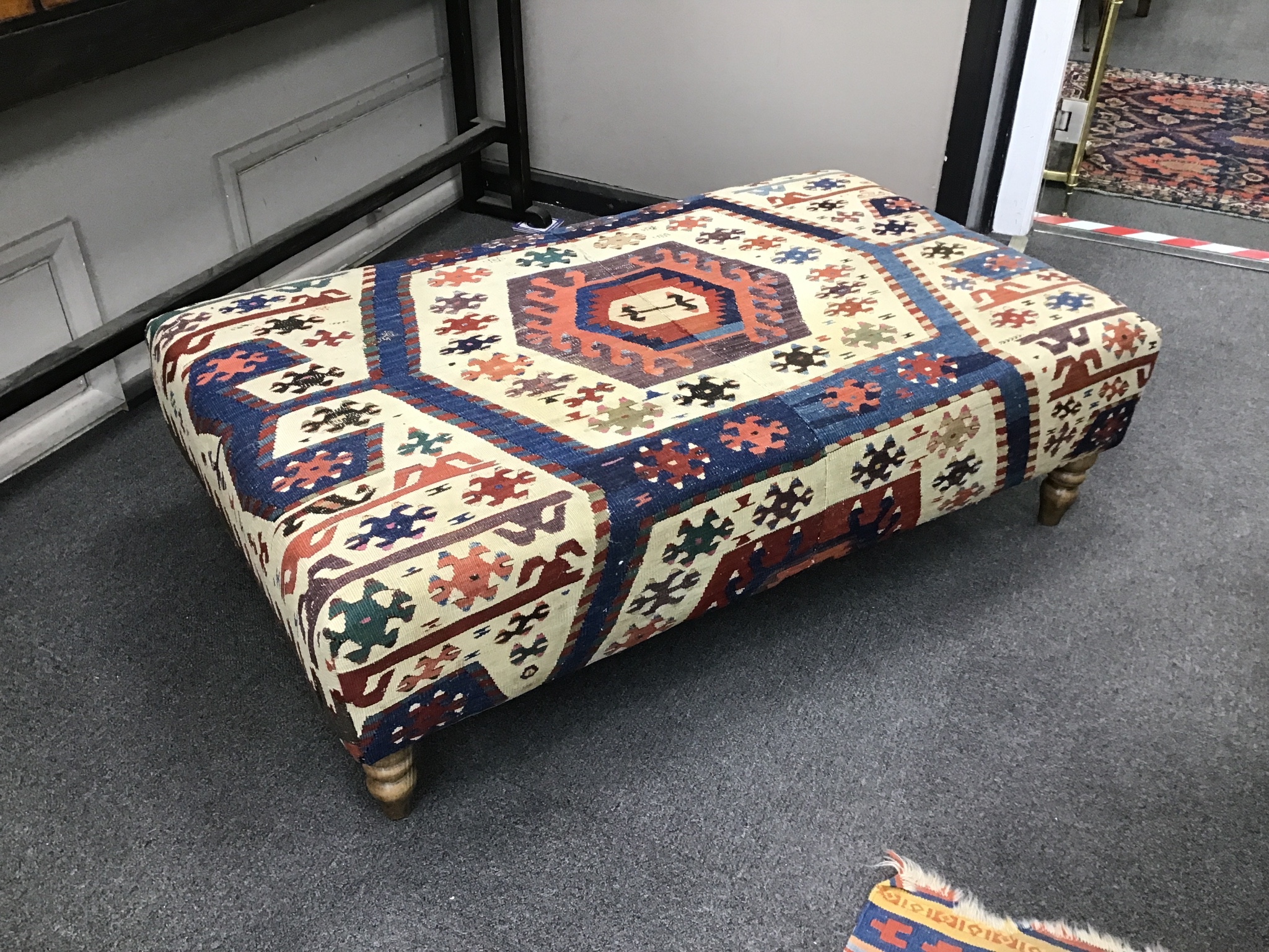 A large rectangular coffee table / footstool with antique kelim upholstery on stained turned beech feet, width 124cm, depth 72cm, height 38cm.